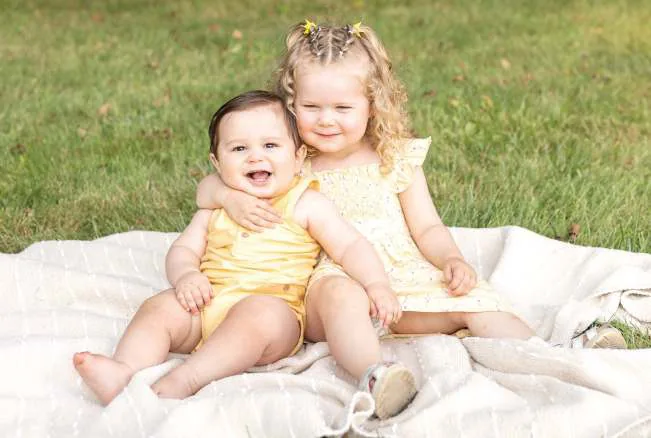 Esmé and Arlo sitting together on a blanket.